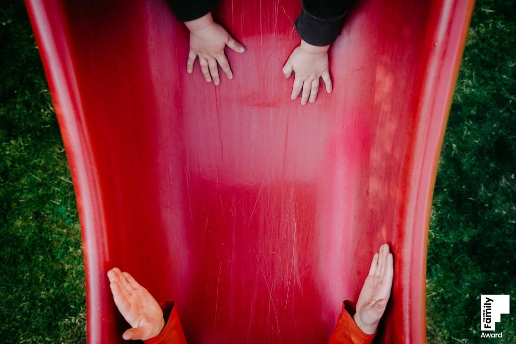 2 Hände fangen 2 andere auf einer roten Rutsche auf I Beste dokumentarische Familienfotografin Sabine Doppelhofer