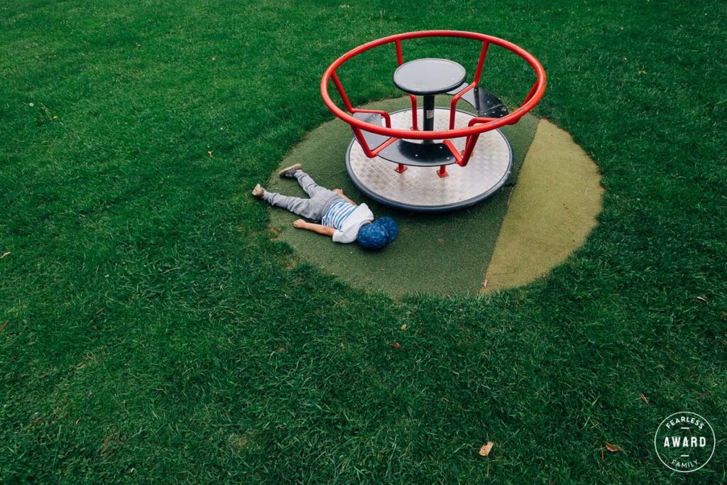 Best Family Photographers Fearless award by Sabine Doppelhofer - Kid lies on green gras on playground